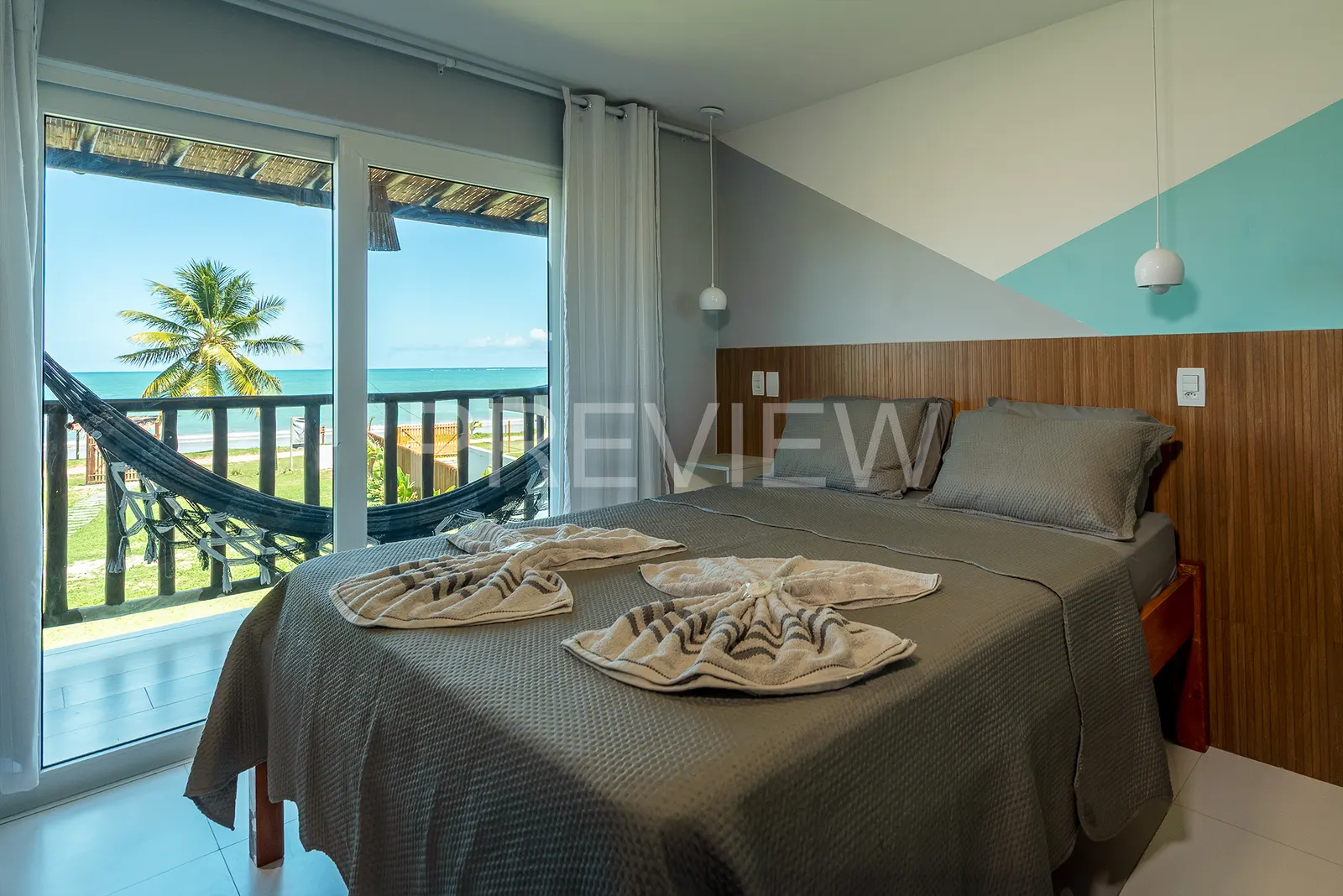 Quarto com cama queen e porta aberta para a varanda com rede e vista para o mar
